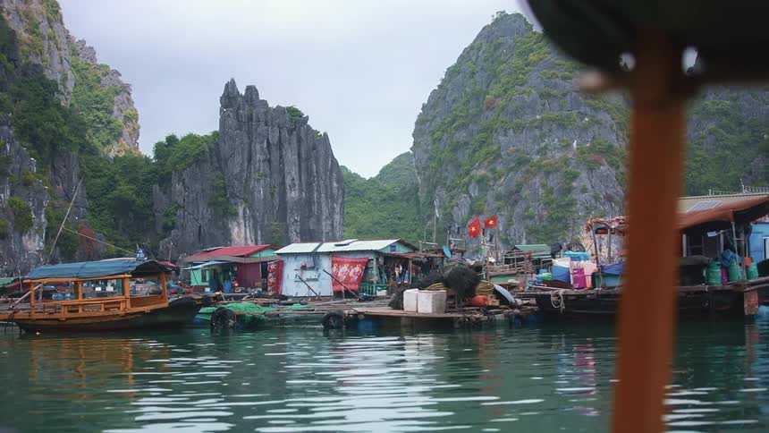 Boat moves past docked boats and houseboats near vegetation covered mountains