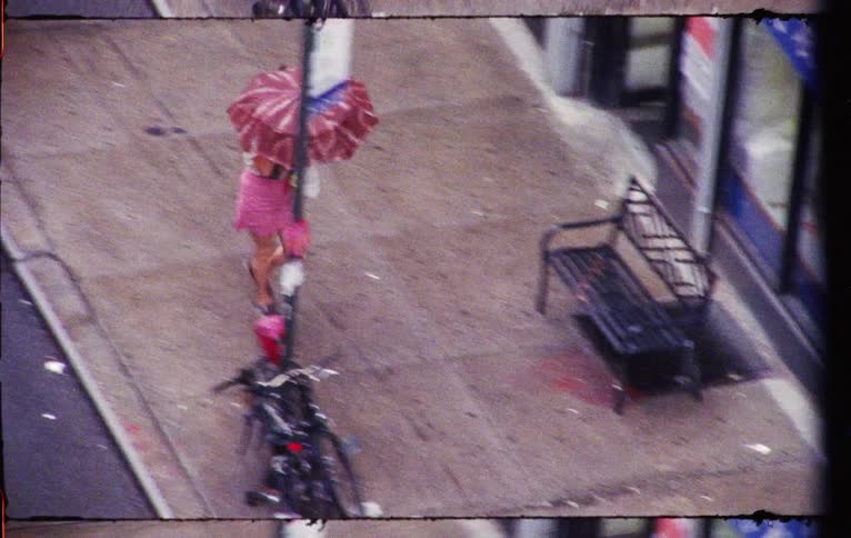 Woman with red umbrella wearing pink shorts walking on the street of a city