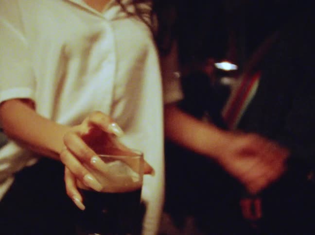 A woman is dancing in a nightclub with other people while holding a glass of stout before she places it on a table