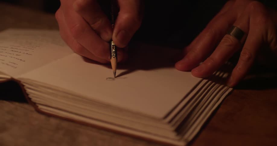 A man draws something in pencil in a book