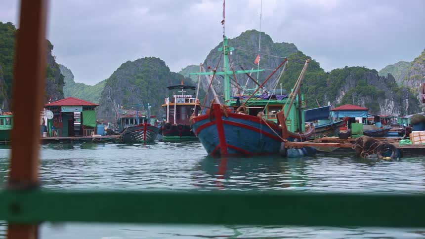 Colorful ships and boats at wooden docks surrounded by mountains under a cloudy sky