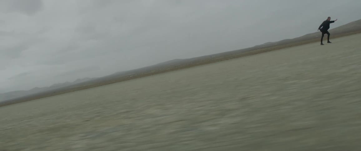 Man wearing all black runs quickly across flat land on a cloudy day