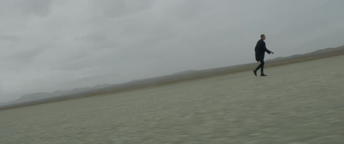 A man is walking across the desert on a cloudy day