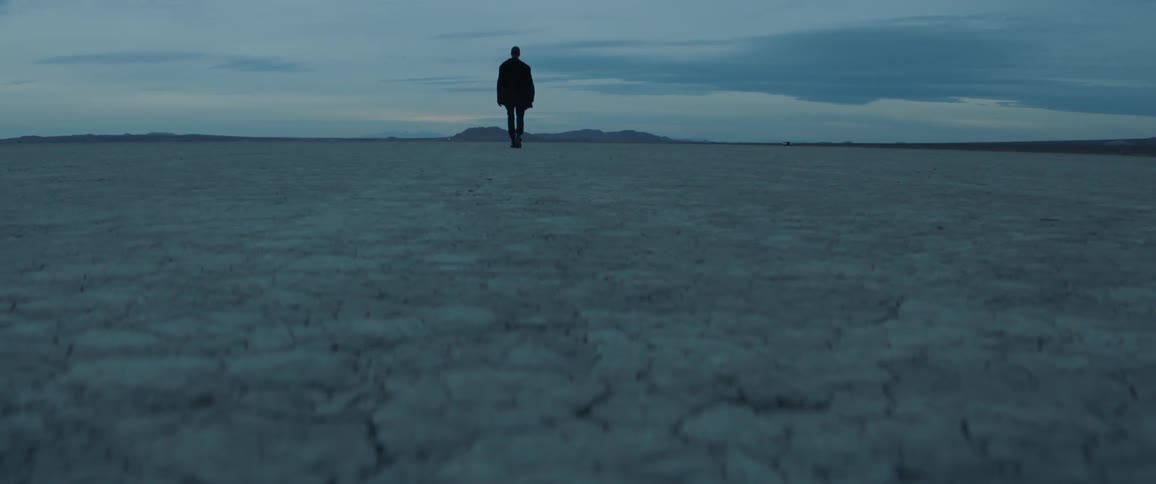 A man walks towards a distant mountain on a cloudy afternoon