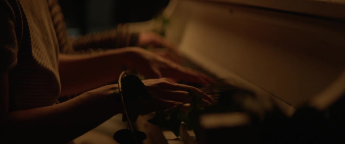 Two people play a piano as vines grow over it