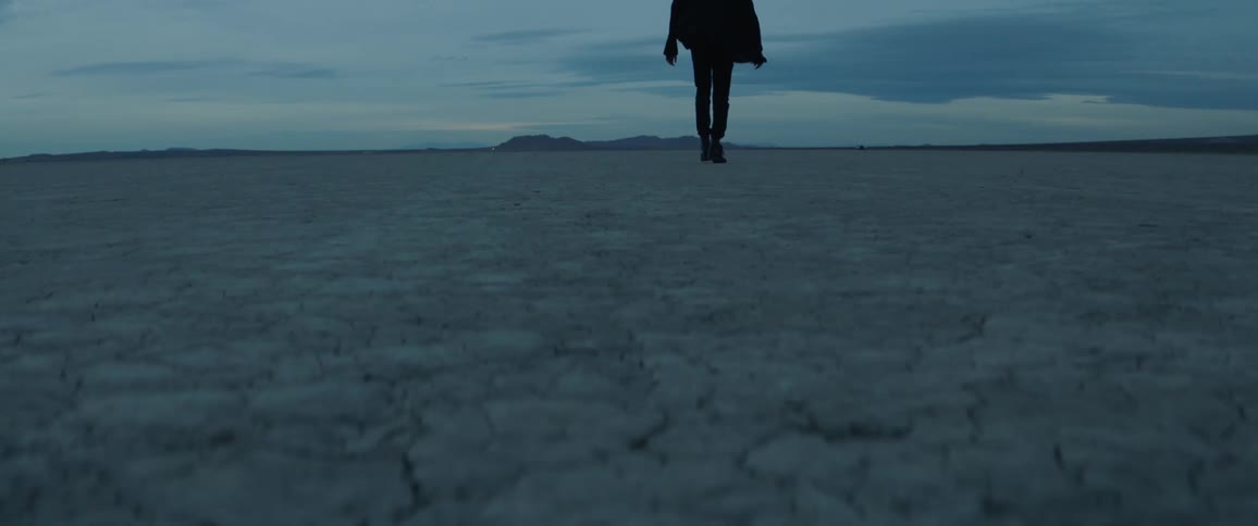A man walks across a desert at dusk