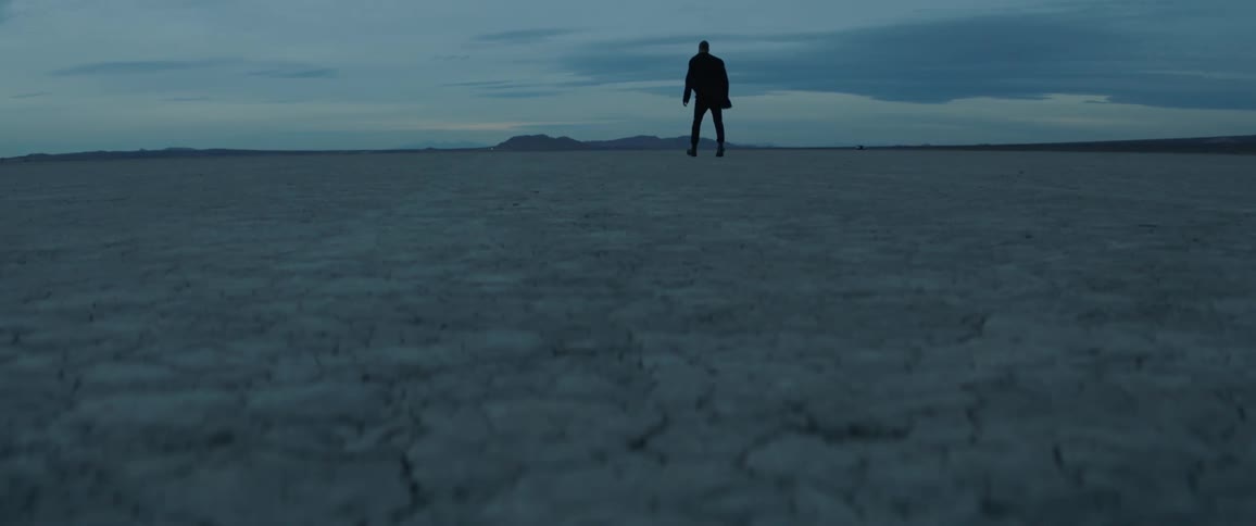 A man walks across a desert at dusk