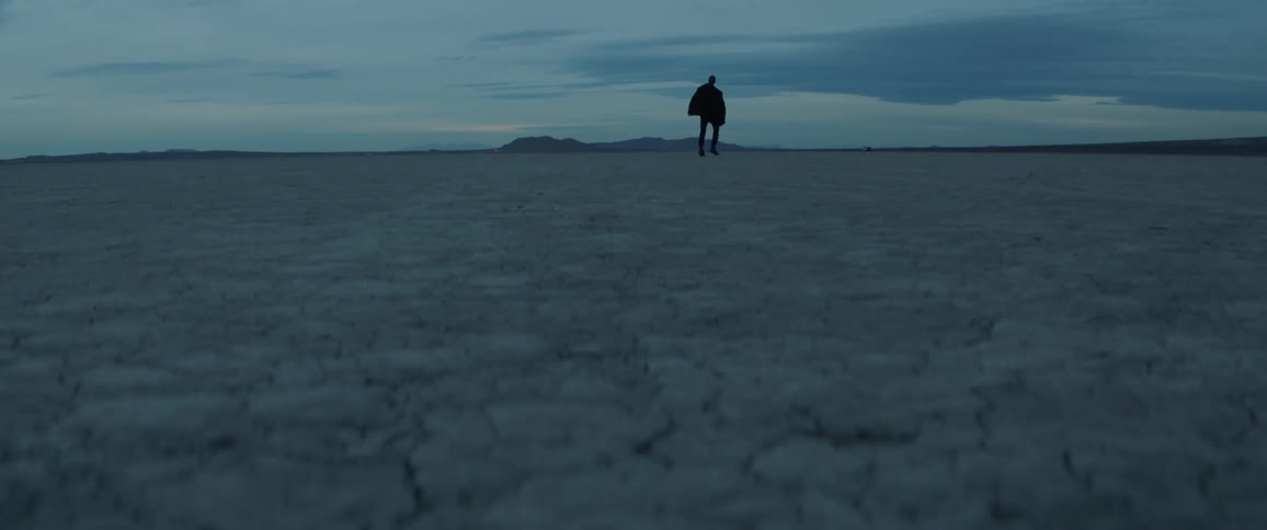Man wearing all black dances on flat plains on a cloudy day