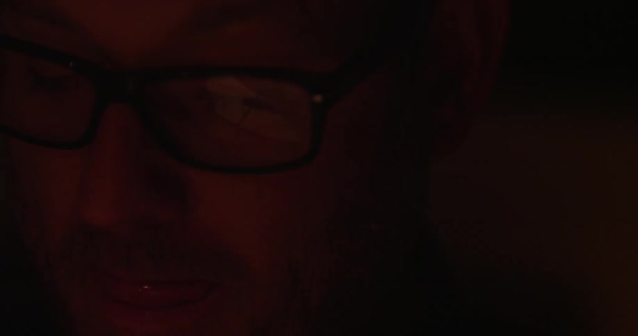 A red glow on the face of a man wearing glasses