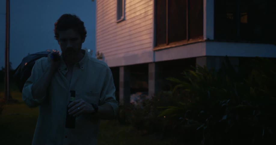 A man carries a beer bottle along with him as he takes out the garbage