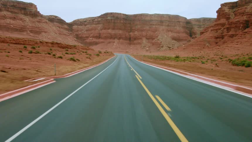 Highway rolls past vegetation dotted desert and buttes