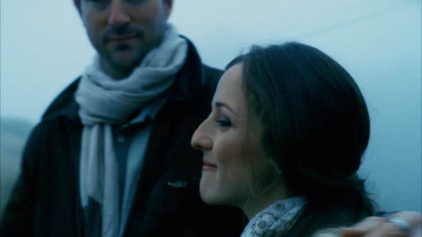A man walks towards a woman and puts his arm around her