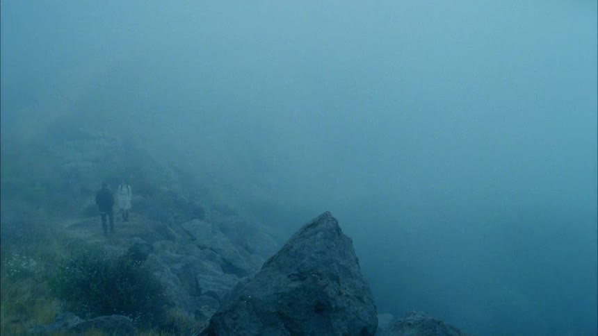 A man walking towards a woman on a cliff with fog