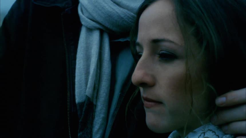 Man with a black overcoat a grey scarf holds and consoles sad woman with a ponytail on a cloudy day