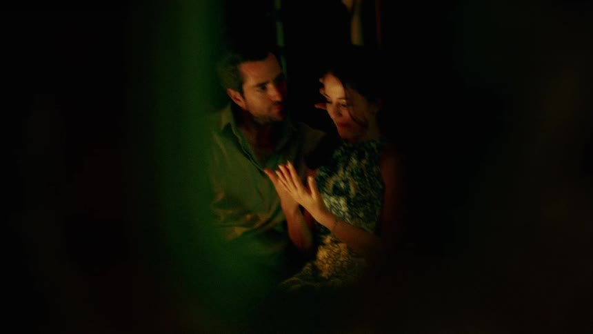 A man and woman sit outside and he leans over and kisses her