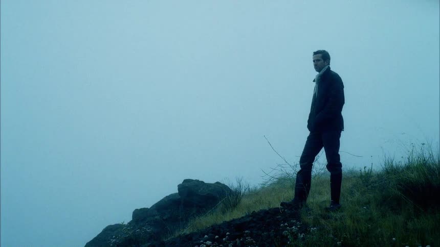 A man stands on a hill amongst thick fog before turning away and descending the hill