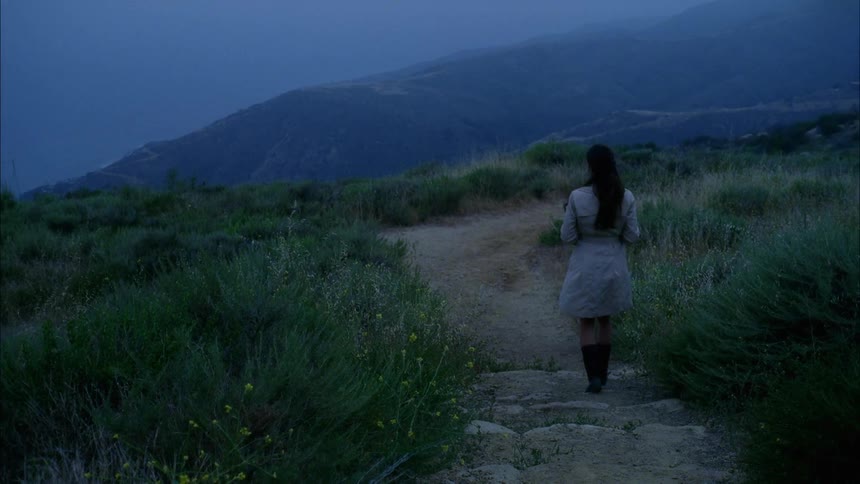 Woman with long hair and wearing a coat walks down the rocky steps on a trail