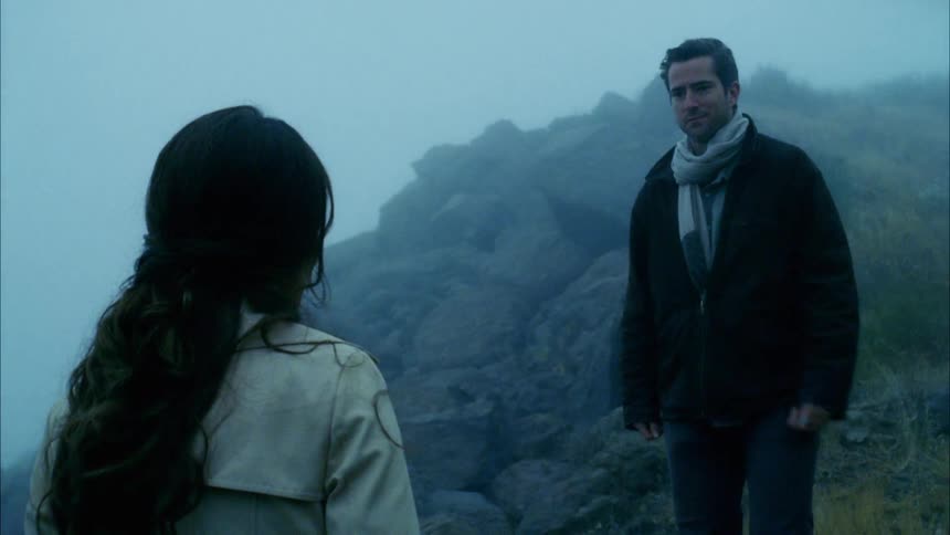 A man comes close to a woman and tenderly touches her face while hiking in a mountain surrounded by mist
