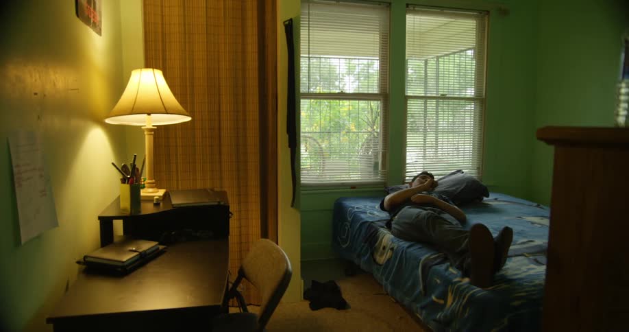 Man with a t shirt and pants lies down on bed in his room
