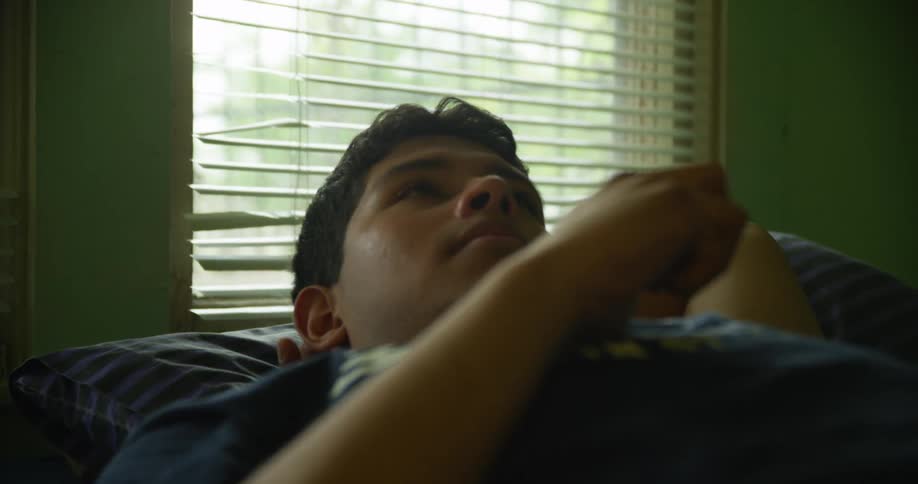 Man deep in thought lies on bed and looks at the ceiling