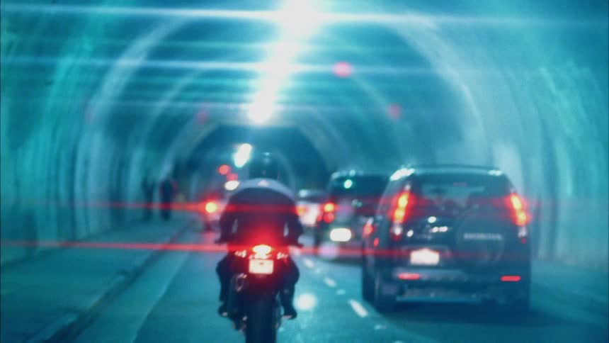 Cars and a motorcycle driving through a tunnel in a city as two pedestrians walk by
