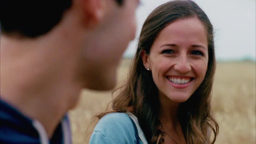 Girls smiles when a man takes her hand while walking on a grass field