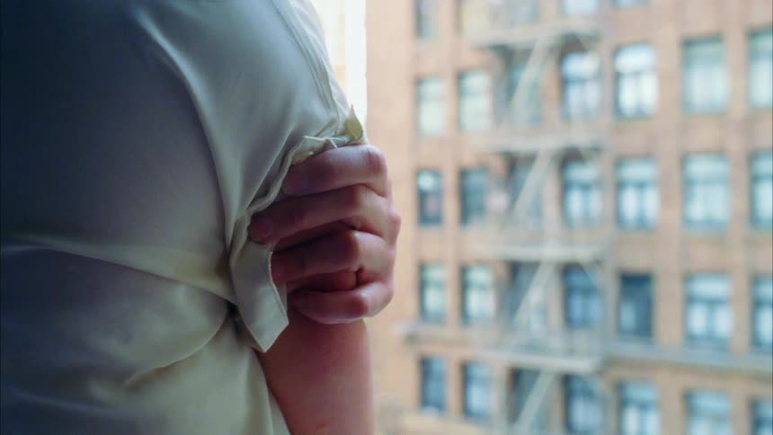 A person rubs their shoulder by the window