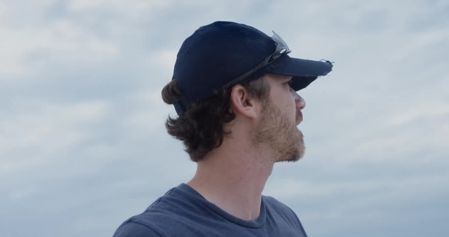 A confused man looks around the area while standing outdoors under a cloudy sky