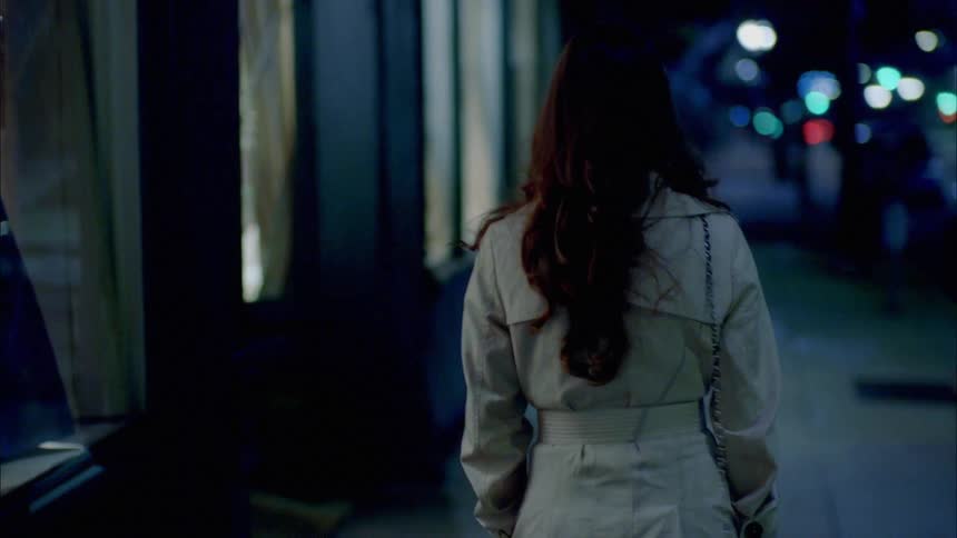 A woman walking past stores on a city street at night