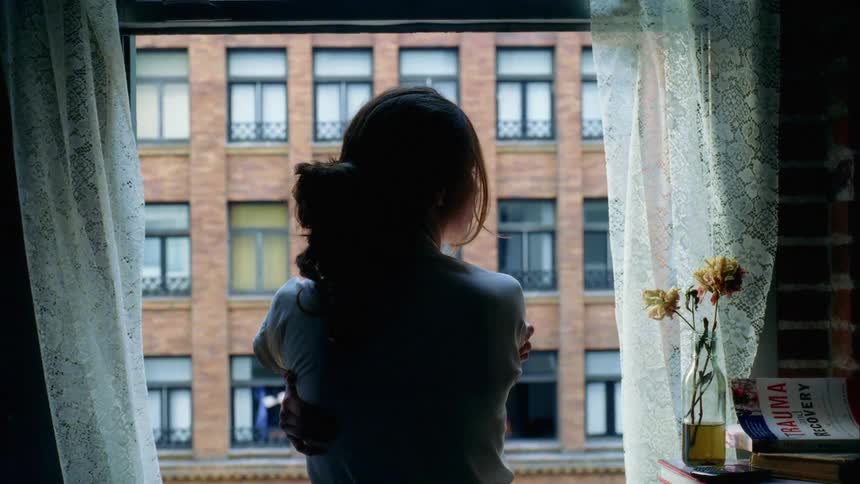 Woman with a ponytail and a white shirt looks out the apartment window