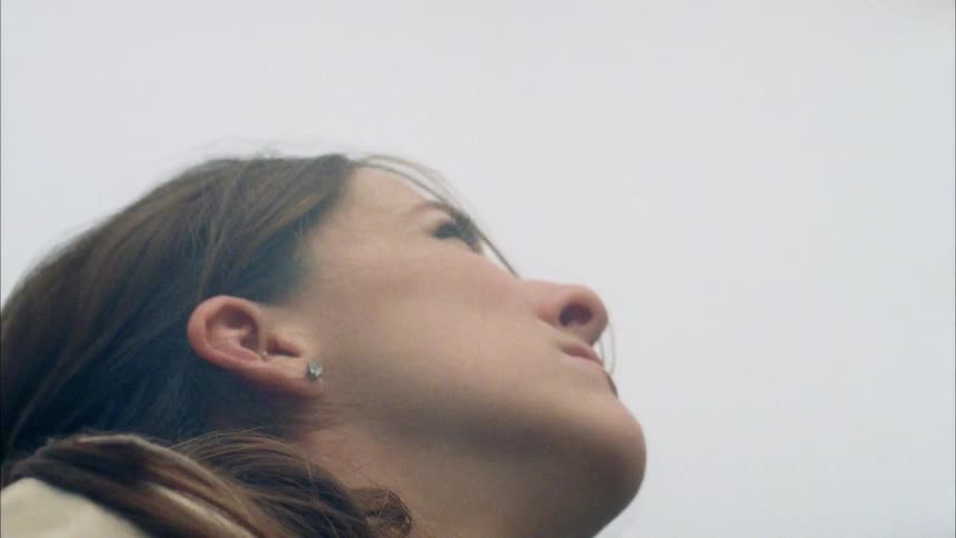 A woman standing outdoors looks up as a small airplane flies overhead