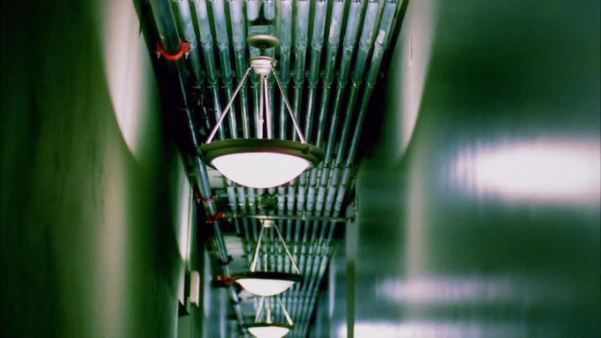 Circular lamps hang from pipes on the ceiling of a long narrow hallway