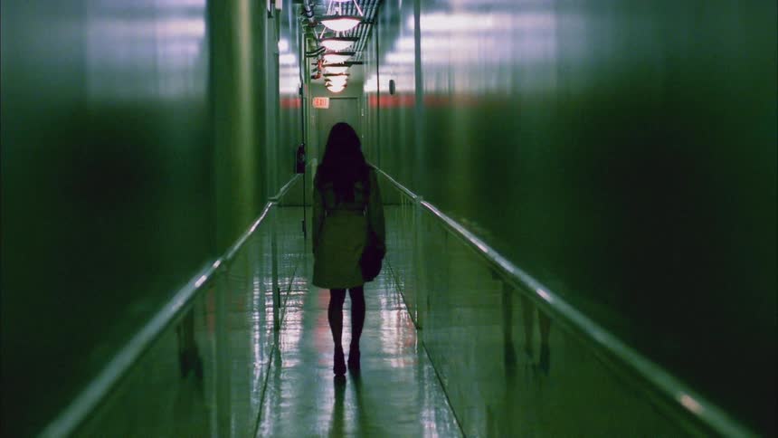 A woman stumbles as she walks down a narrow dimly lit hallway