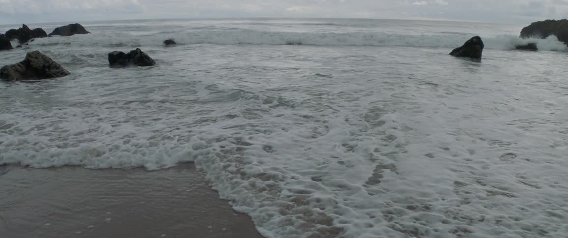 Waves crash against the shore on a cloudy day