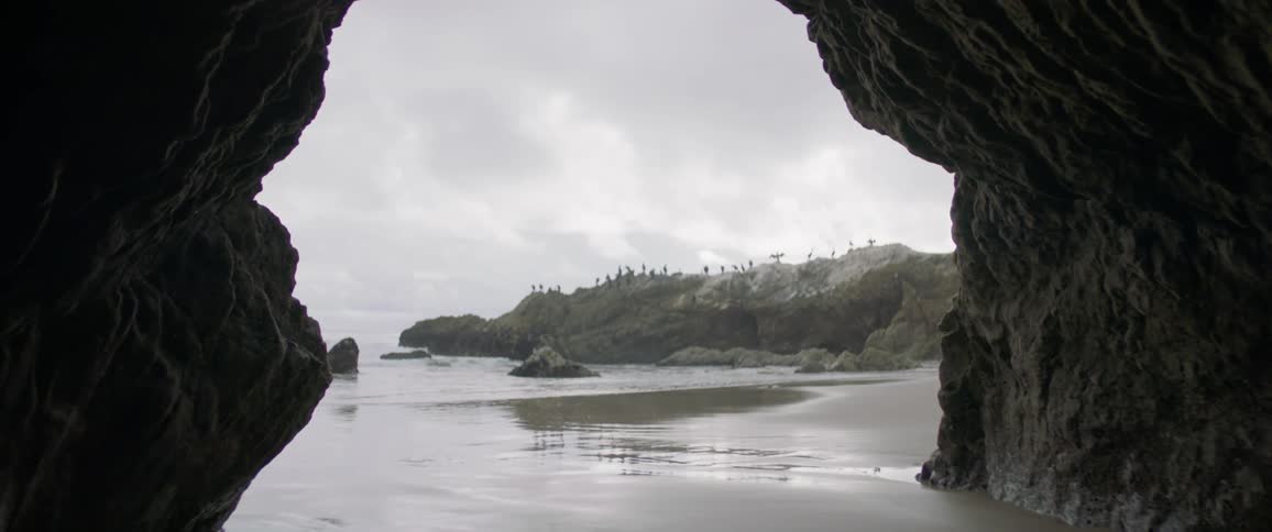 Water flows onto the shore in front of a cave