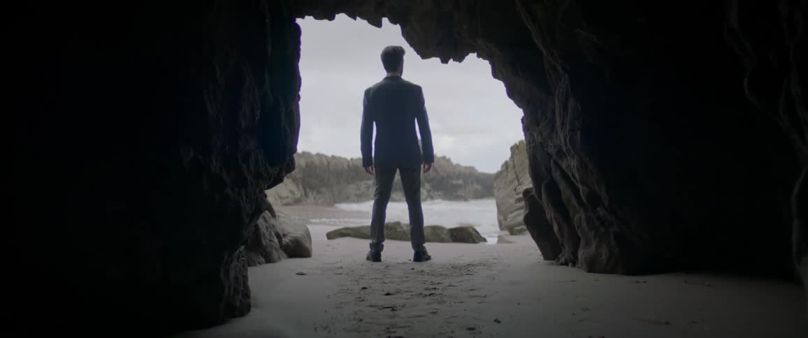 A man stands by the foot of a cave near the beach