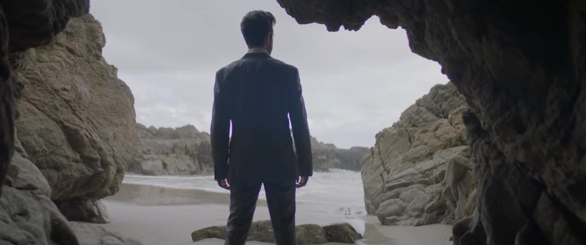 Man standing in the mouth of a cave looking at a body of water