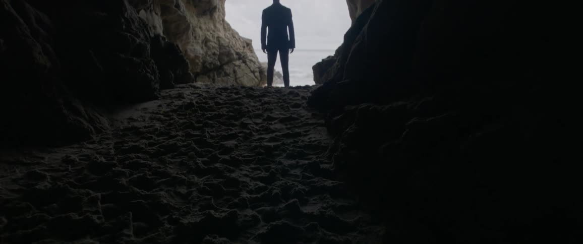 The sand in the cave is dark leading to a man standing ahead
