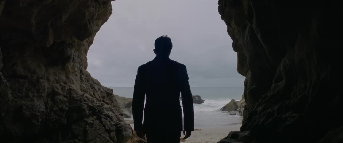 A man walks through a cave toward the ocean
