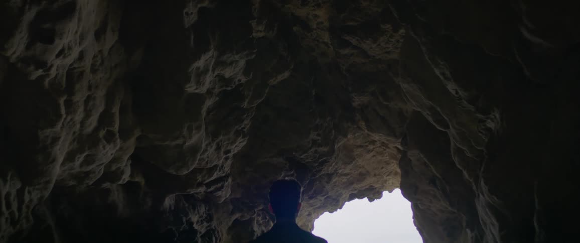 A man walks through a cavern towards an opening