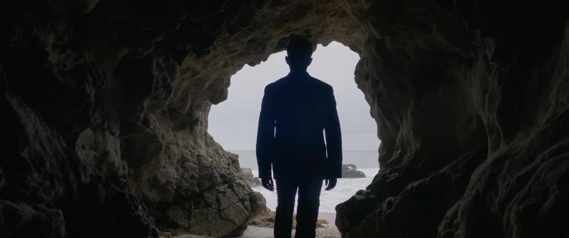A man walks through the cave towards the ocean