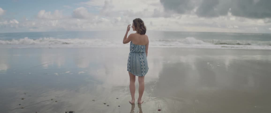 A woman stands barefoot on the wet sand