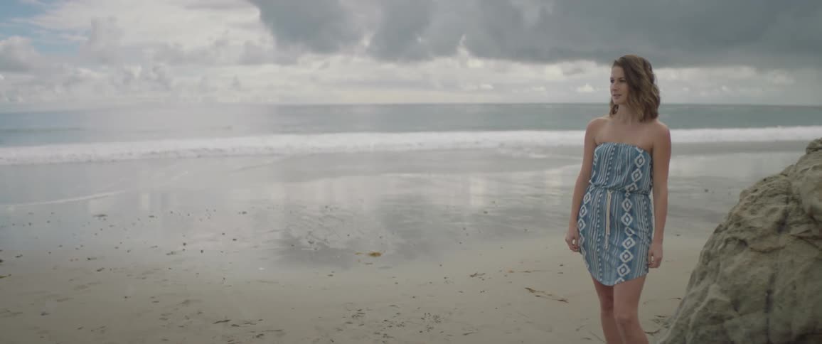 A woman is standing on the beach with her back to the ocean