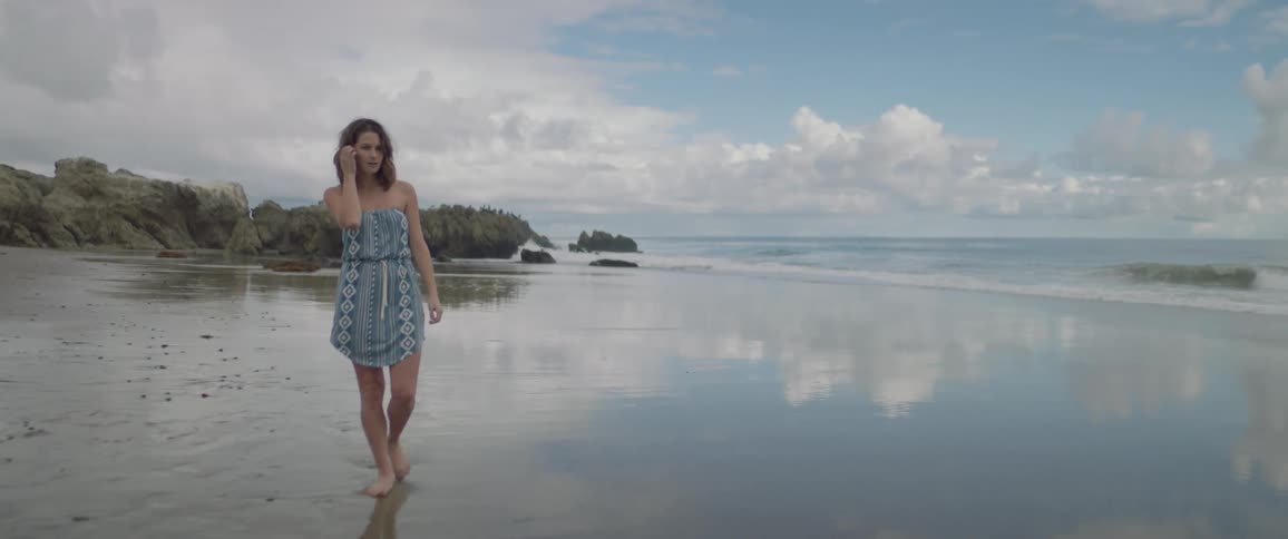 The waves slowly hit the shore of a beach as a woman walks by