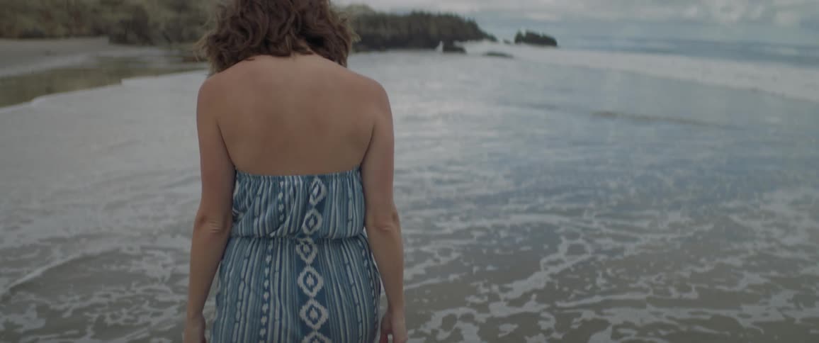 A woman walks along the beach and into the water on a cloudy day