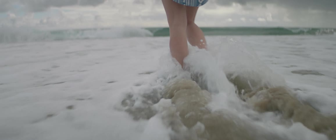 Woman walks barefoot over the sand and into the water