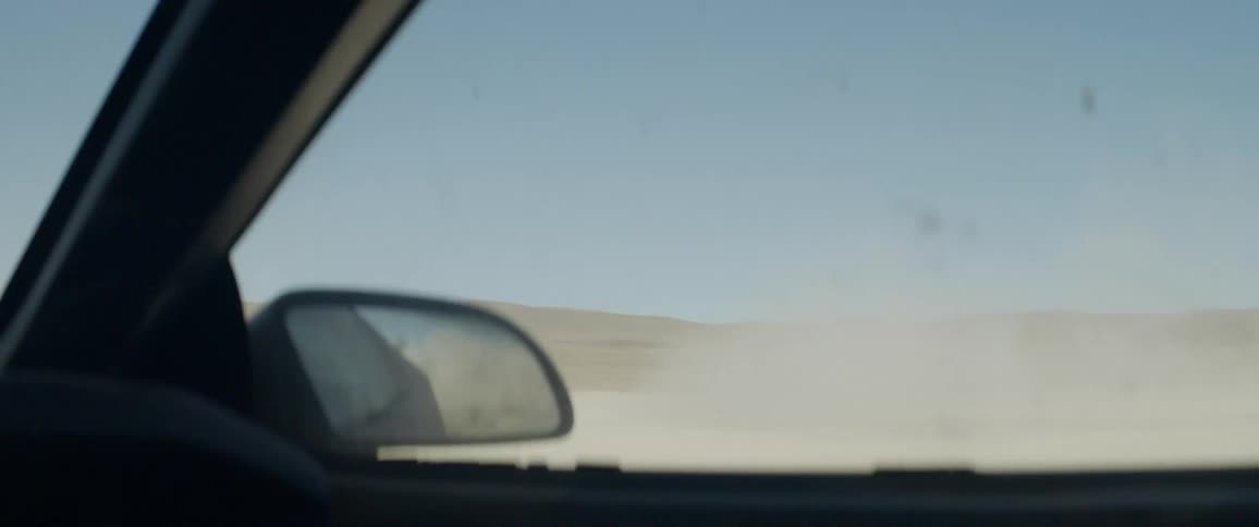 A vehicle is kicking up dust as it does circles in the desert during the day