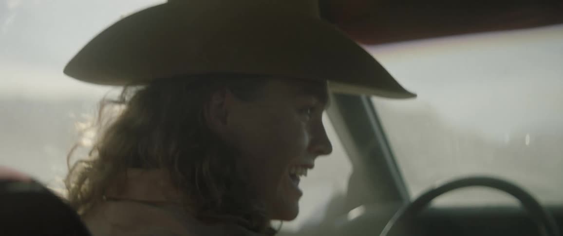 A woman puts on a cowboy hat and laughs while steering a car