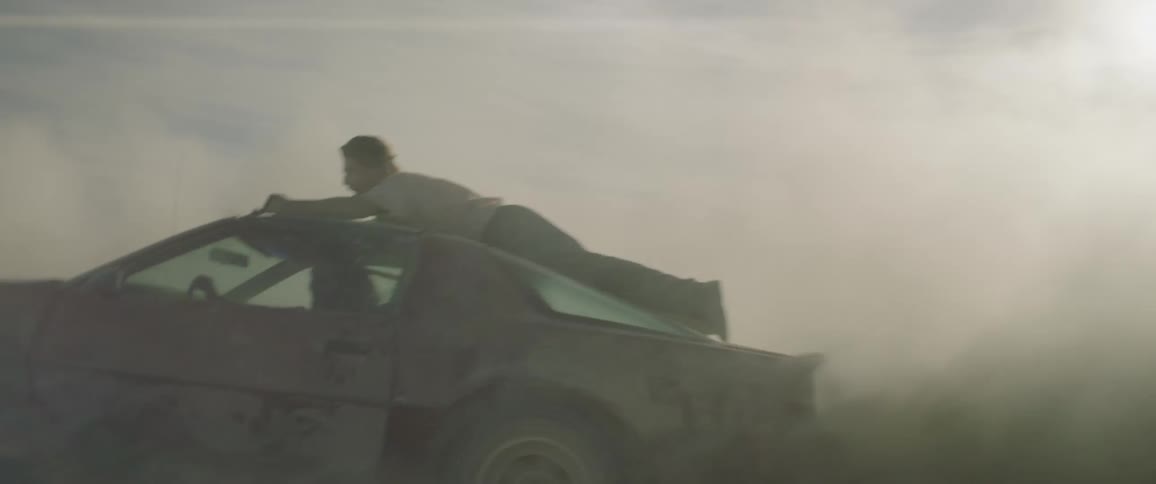 Man rides on the roof of a dusty red car