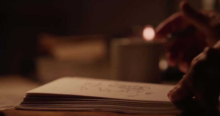 A person draws in a notebook and sips from a mug